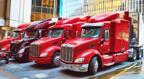 Red semi-trucks parked in a city setting, with a focus on the front of the vehicles.