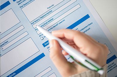 Hand holding a pen filling out a form with blue and white sections.