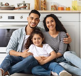 Family smiling, sitting on the floor in a kitchen. Father, mother, and child looking at the camera.