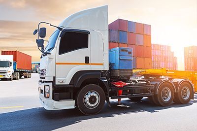 White semi-truck hauling shipping containers on a road, sunny outdoor setting.