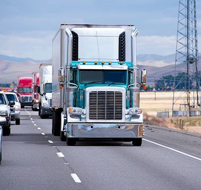 Semi-trucks driving on a highway; blue and silver truck in the foreground, other vehicles in the background.