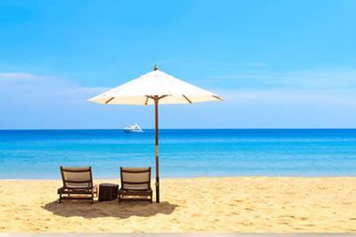 Two beach chairs under a white umbrella on a sandy beach, blue ocean, and sky.