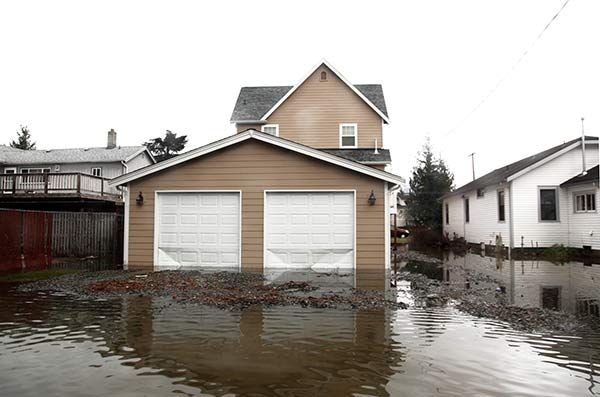 Flood water surrounds houses, a two-car garage in the foreground, flooding the front yard.