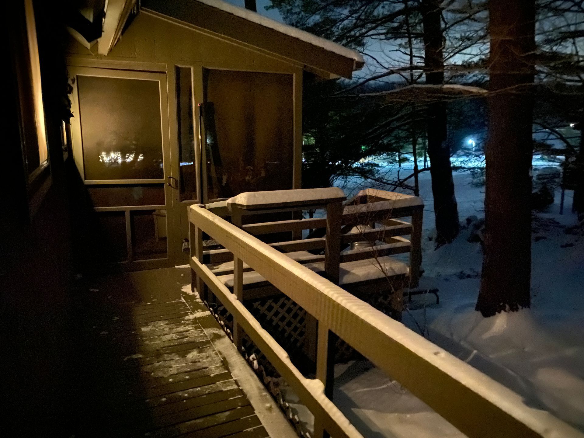 Snowy porch at night; wooden railing, frosted door, trees and cars visible in the dark.