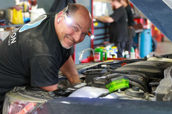 Mechanic inspecting a maroon car with open hood in an auto repair shop
