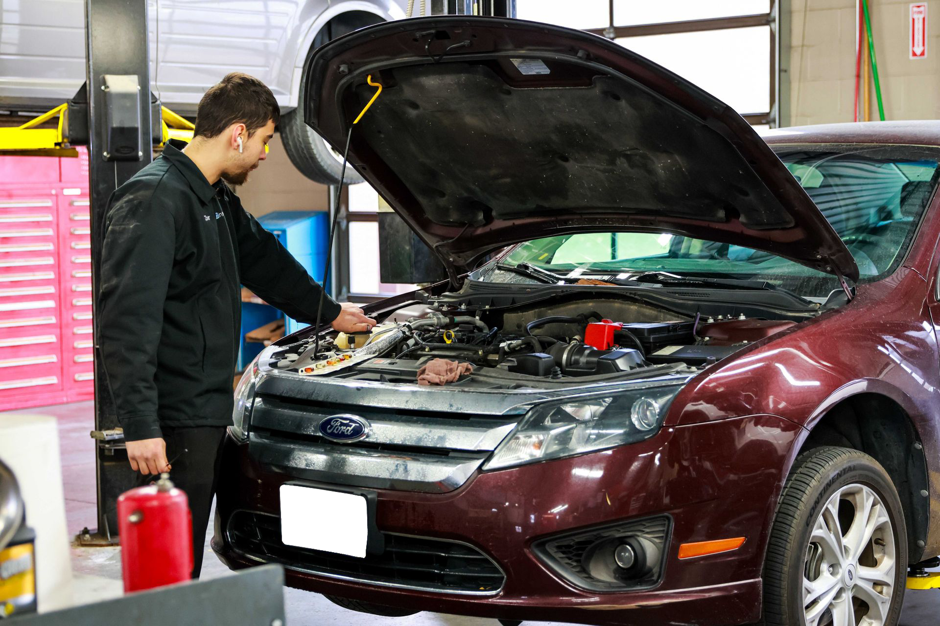 Mechanic inspecting a maroon car with open hood in an auto repair shop
