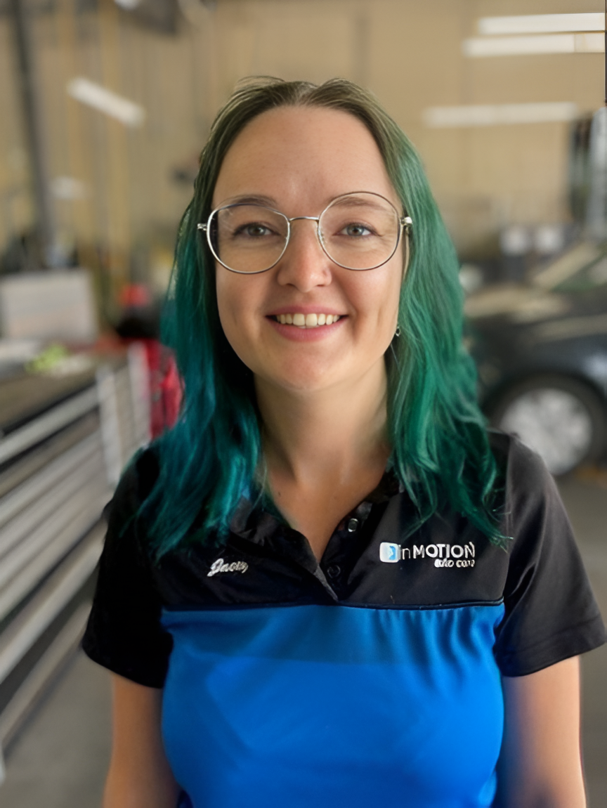 Smiling person with teal hair and glasses wearing a blue and black polo indoors