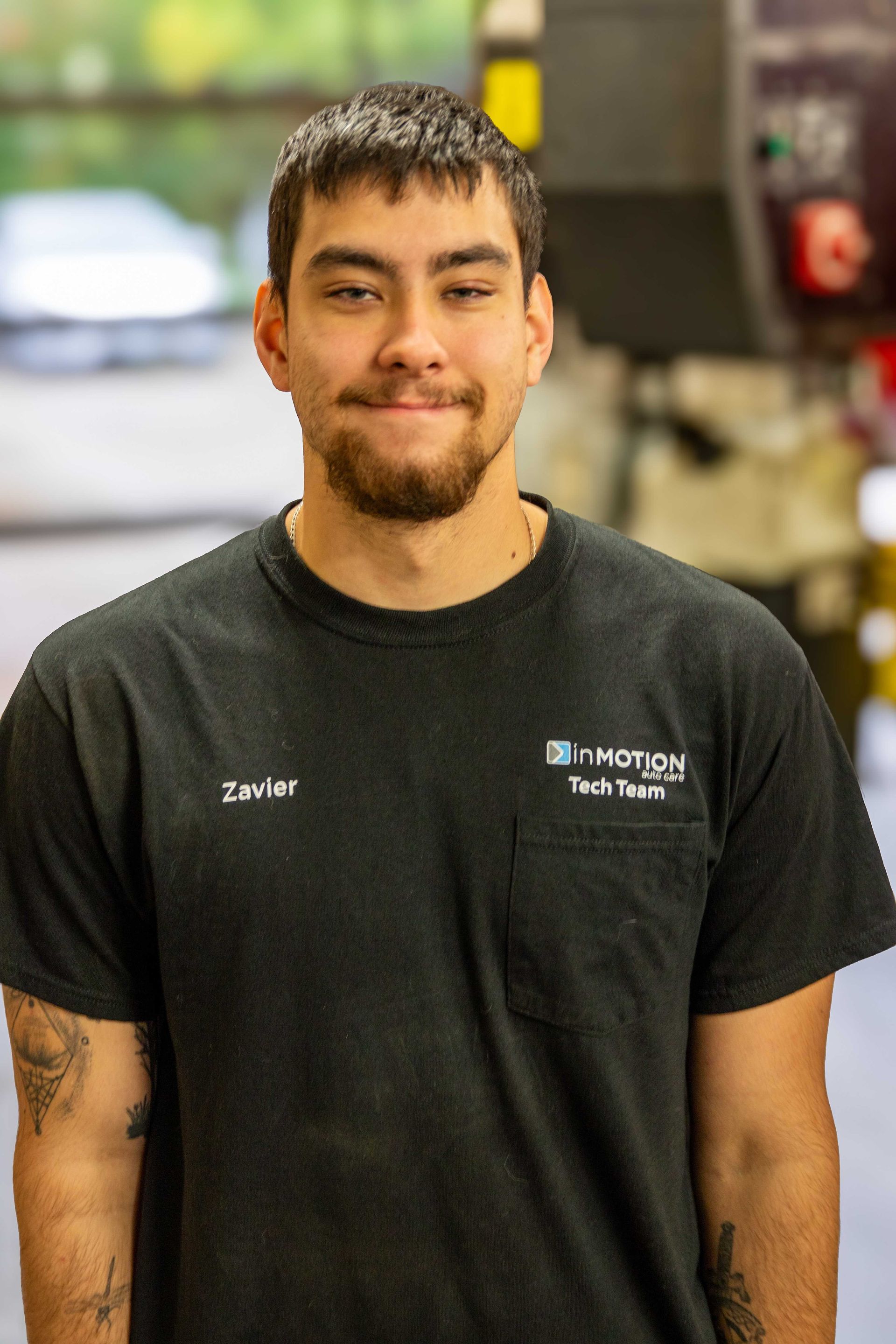Smiling employee in a black T-shirt standing indoors in a workshop or store aisle