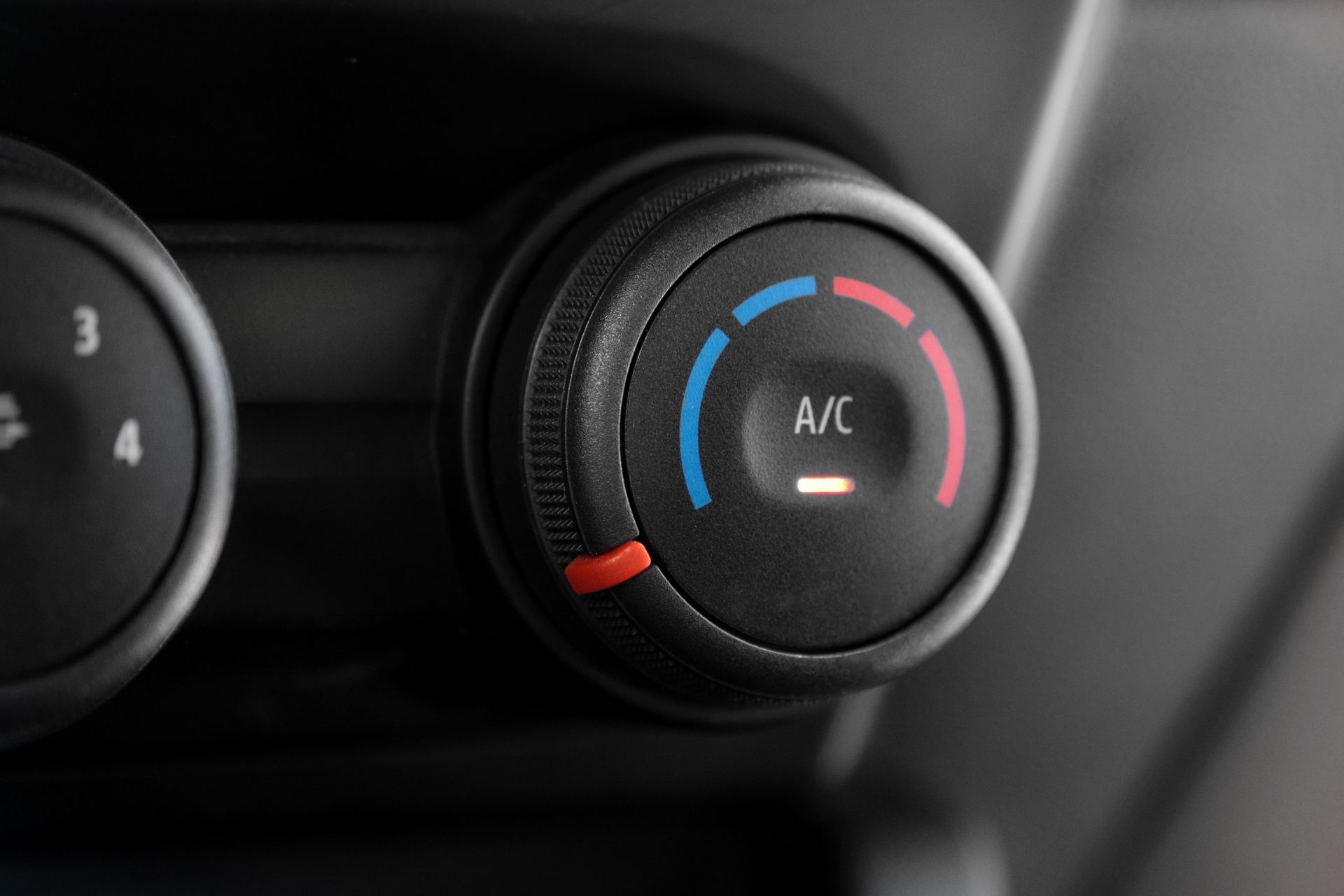 Close-up of car climate control knob with blue and red temperature markings and A/C label