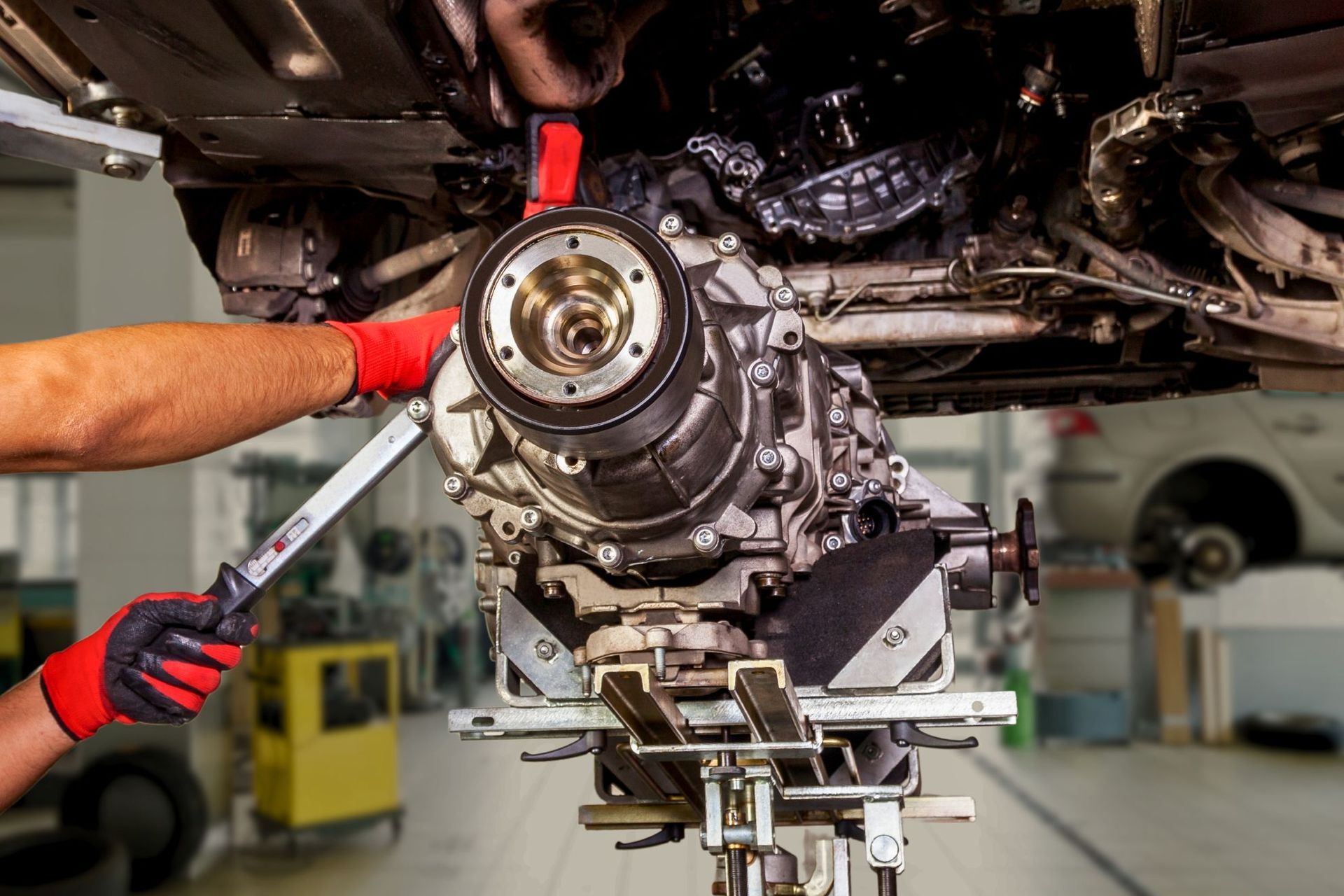 Mechanic tightening a car drivetrain component under the vehicle with a wrench