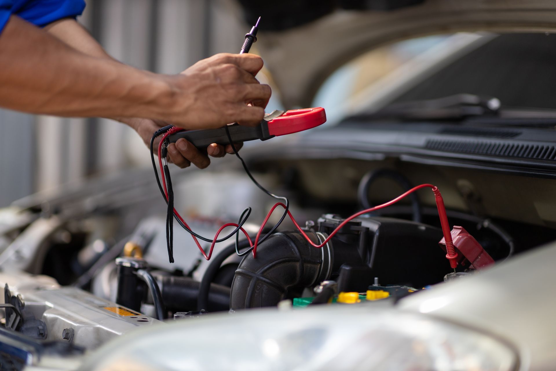 Mechanic using a multimeter to test car battery wires in an open engine bay