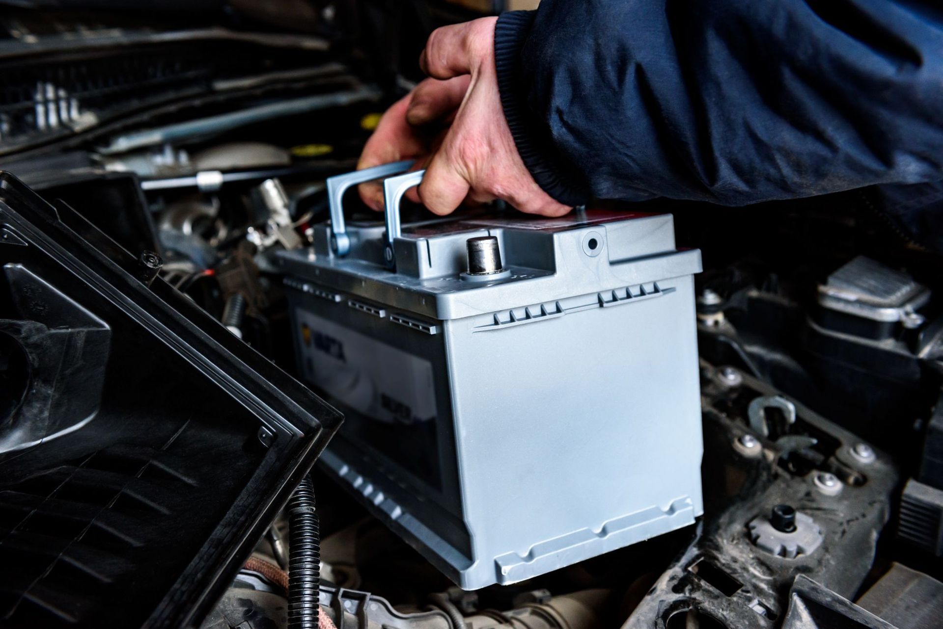 Hand placing a car battery into an engine bay under the hood