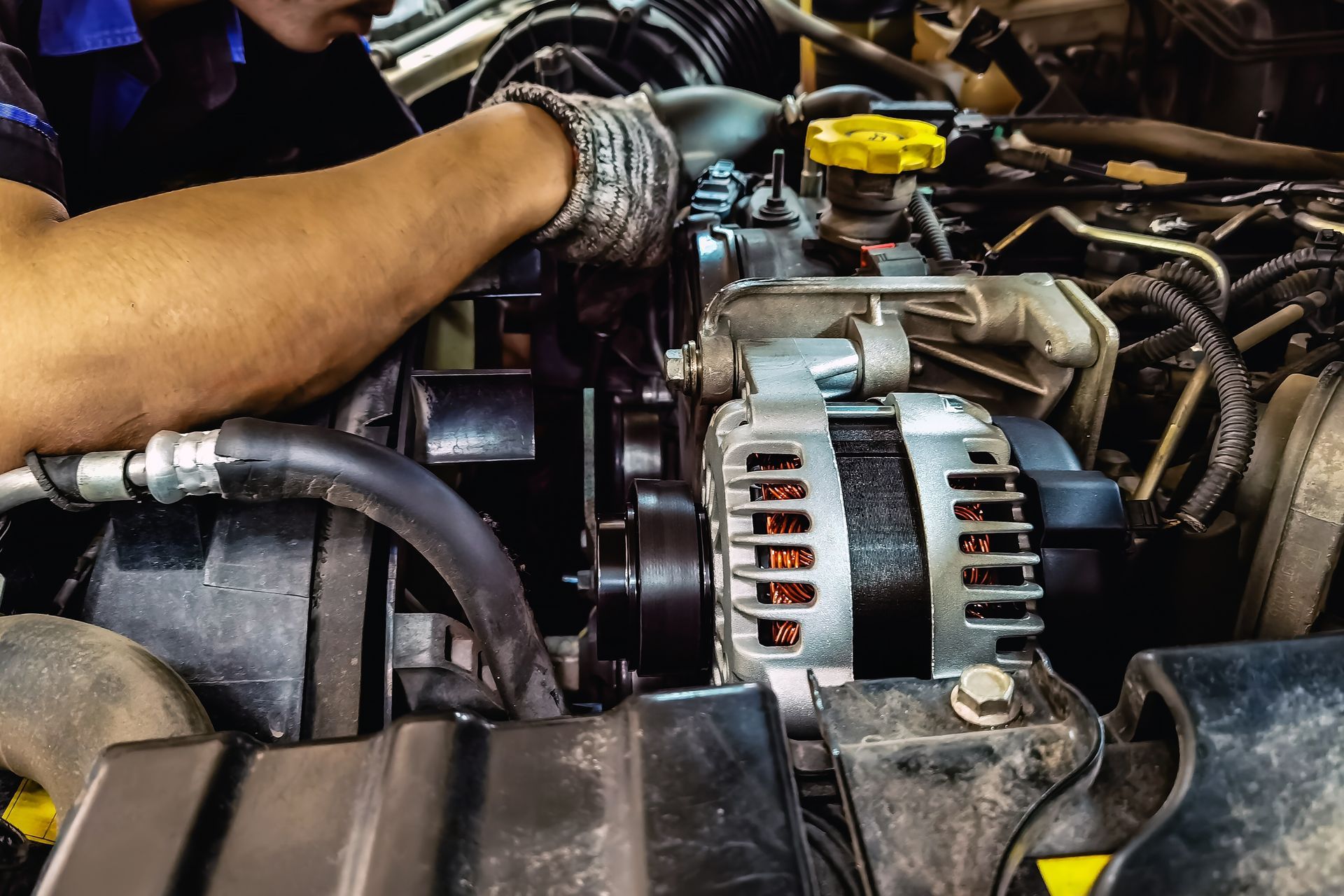 Mechanic’s gloved hands working on a car engine with the alternator visible
