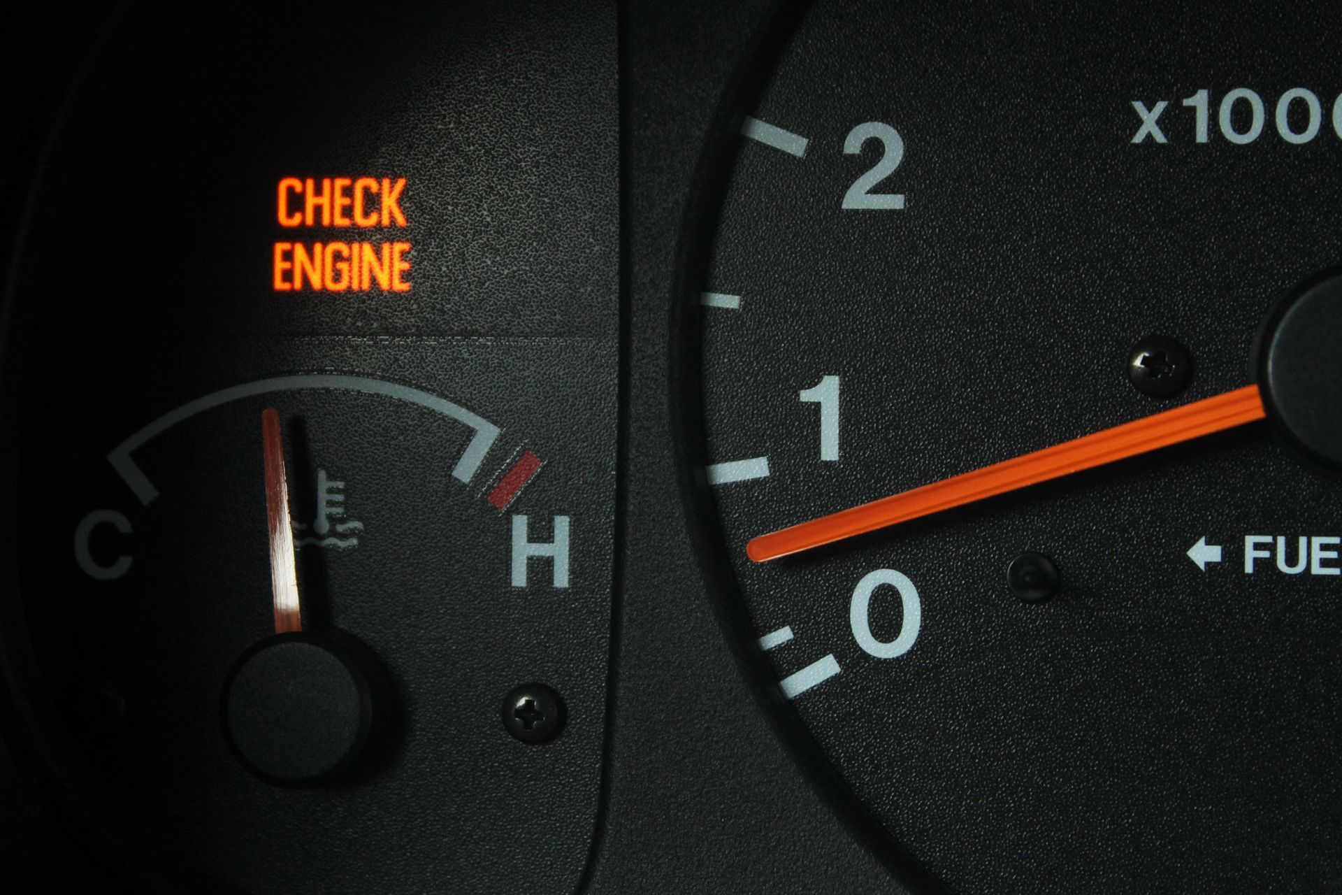 Car dashboard with glowing orange check engine light and fuel gauge needle near empty