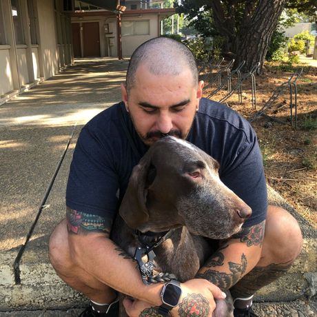 a man with tattoos is kneeling down with his dog