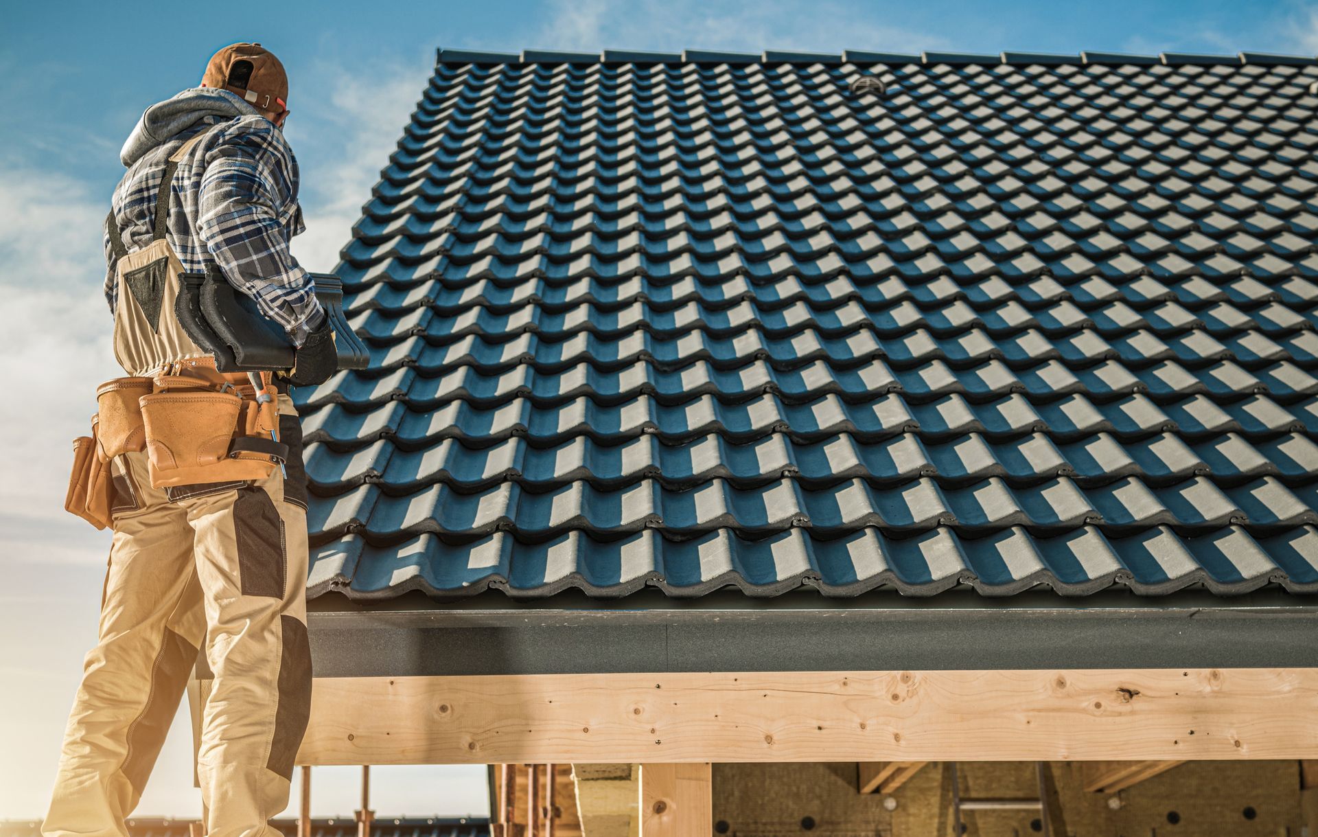 Construction worker installing black metal roofing tiles on a new residential house.