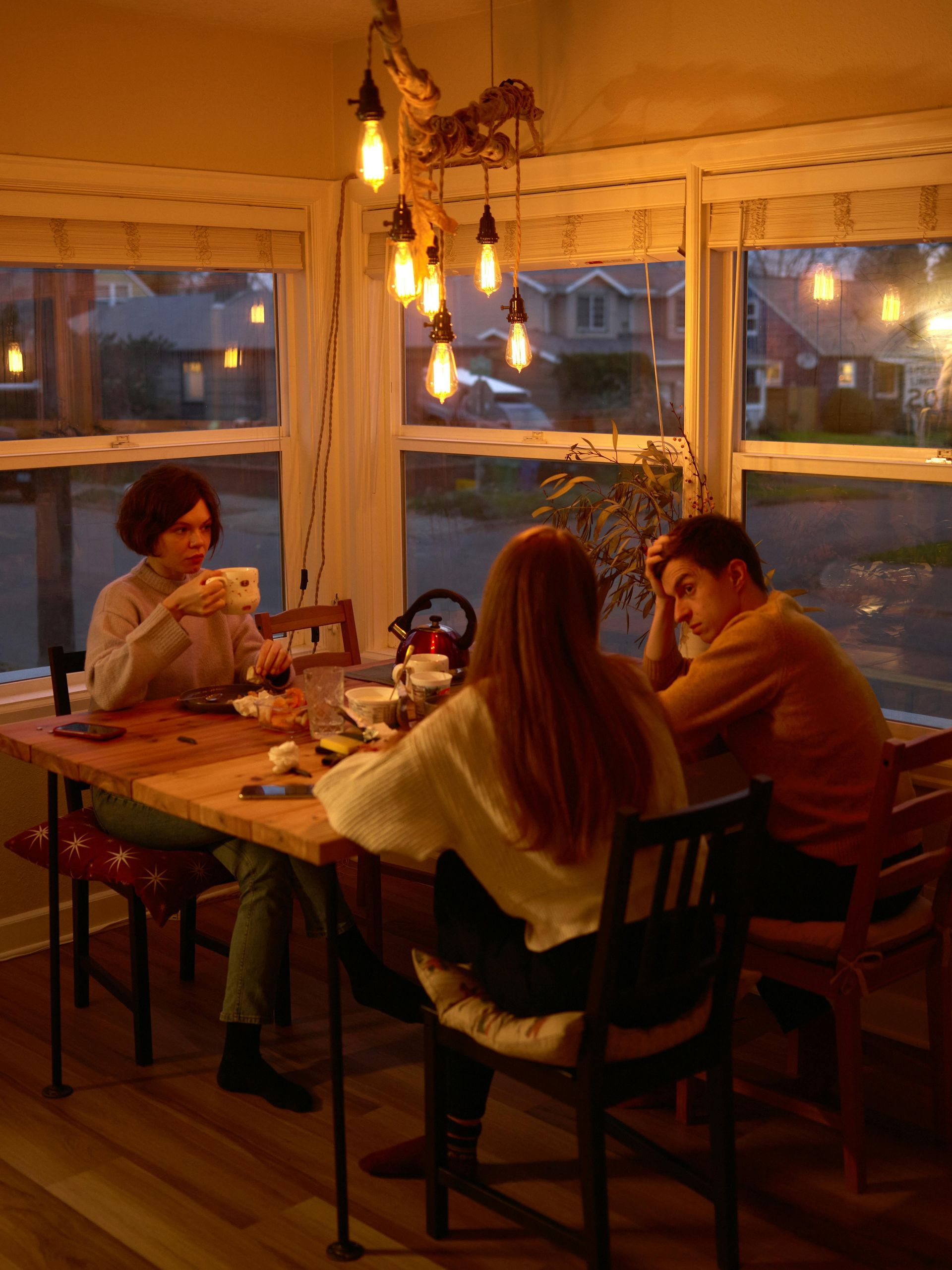 Three people at a wooden table, eating in a warmly lit dining area.