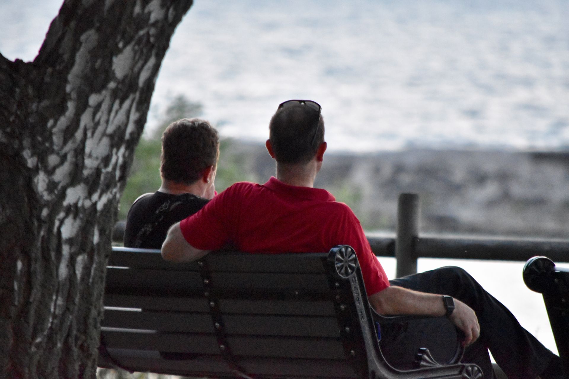 Two men sit on a park bench, facing a body of water.