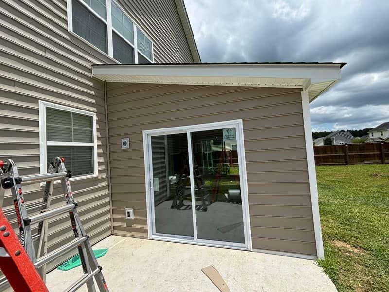 A ladder is sitting on the side of a house next to a sliding glass door.