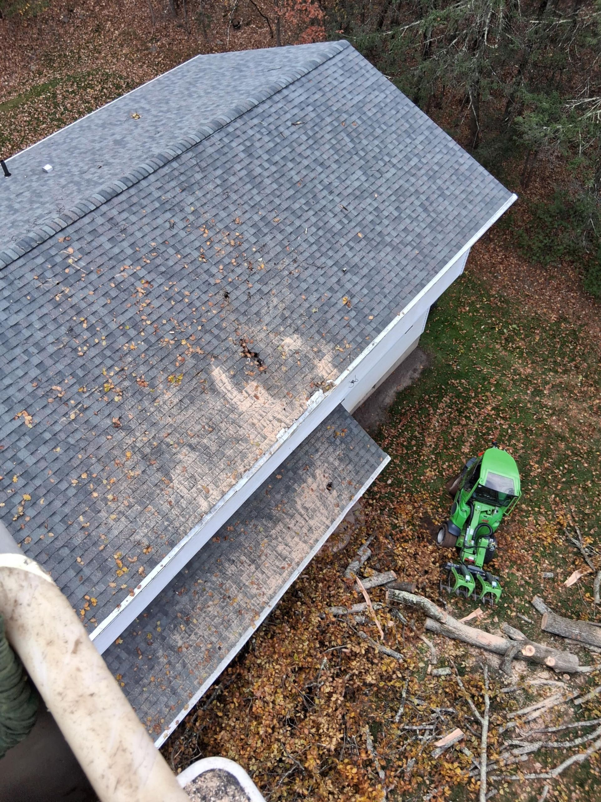 House roof with gray shingles, debris, and a green lawnmower.