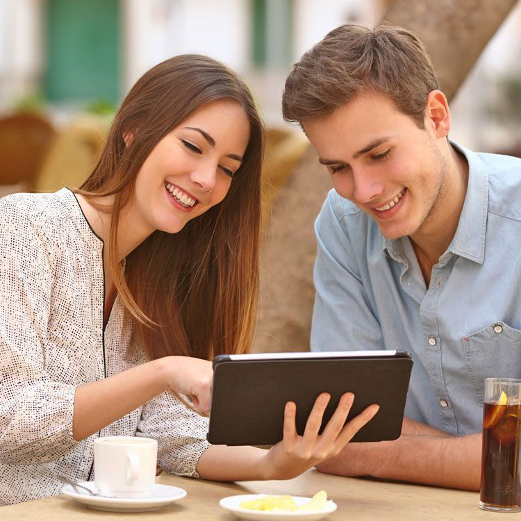 A man and a woman are sitting at a table looking at a tablet