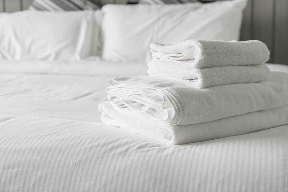 Stack of White Linen Sheets and Towels on Bed — Gold Coast Linen Hire in Tugun, QLD