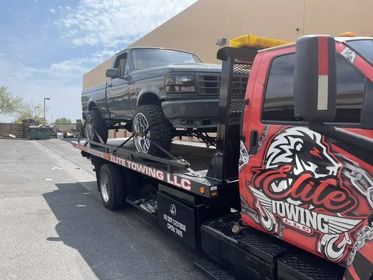 A tow truck is carrying a truck on the back of it.