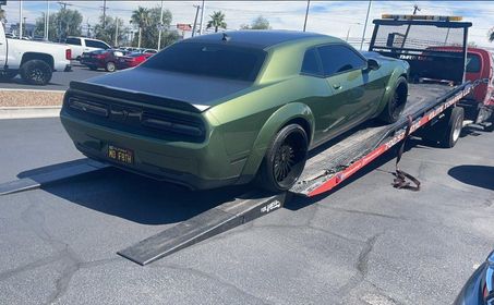 A green dodge challenger is being towed by a tow truck.