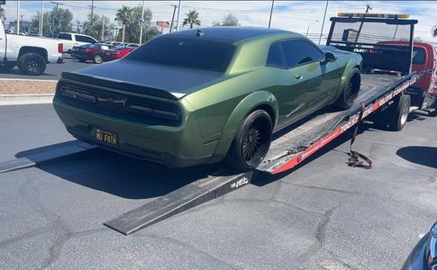 A green dodge challenger is being towed by a tow truck.