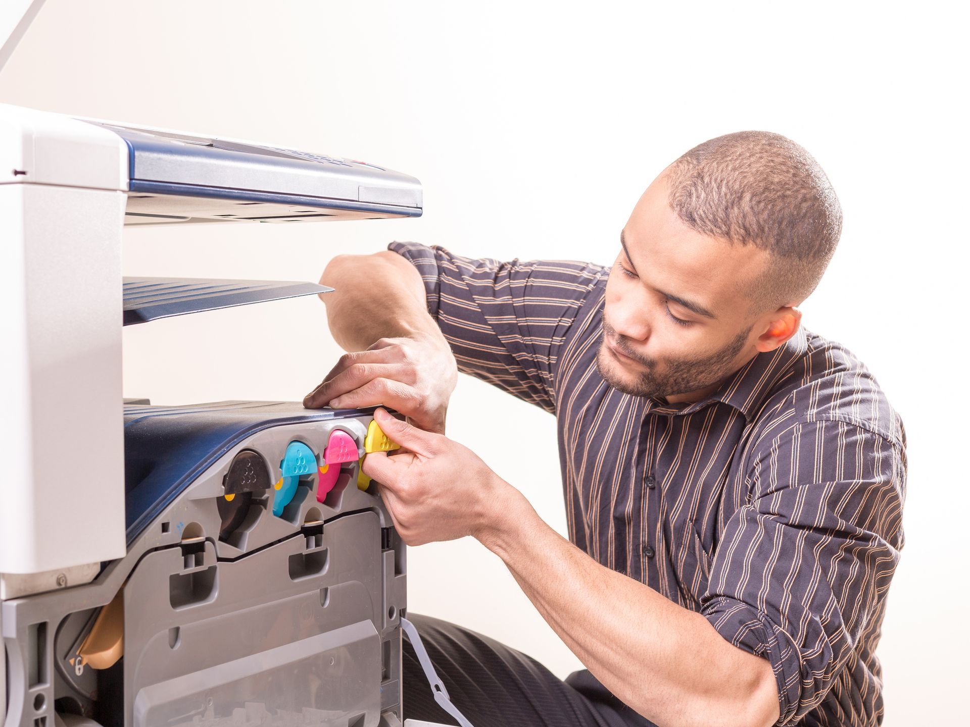 Man repairing a color printer, inserting a yellow cartridge. Indoors, focused expression.
