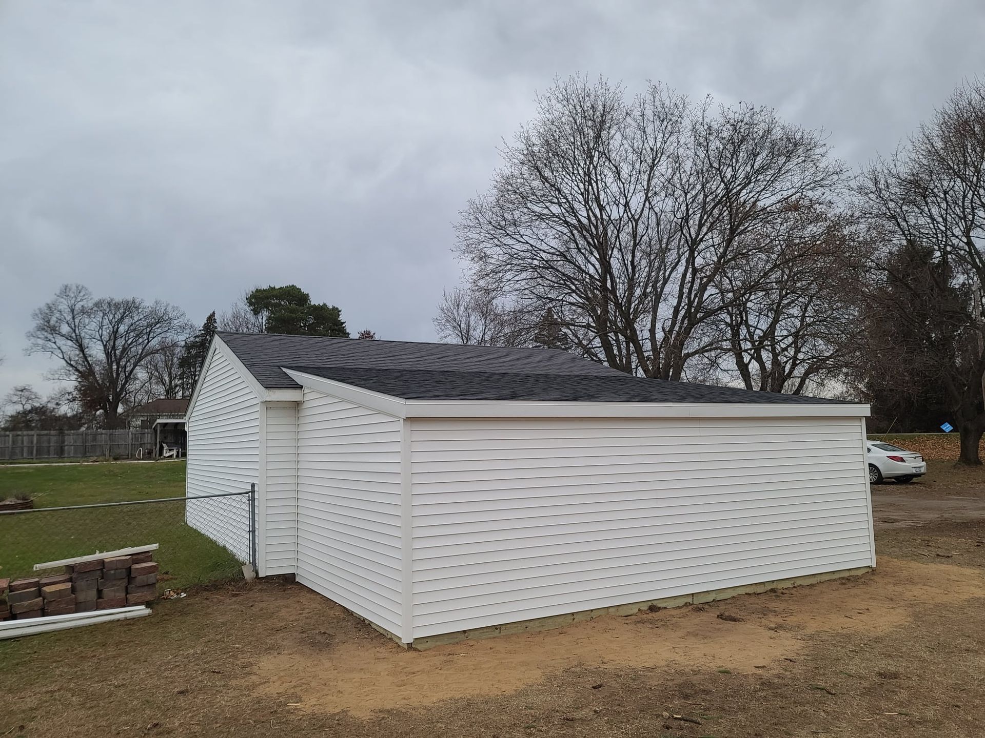 White-sided building with a dark roof on a cloudy day. Construction materials sit on the ground nearby.