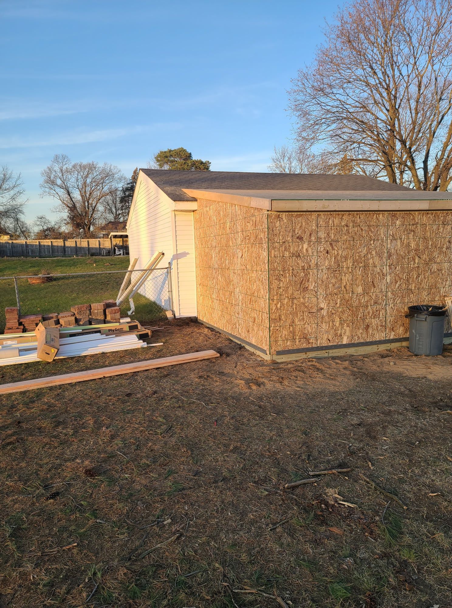 A shed under construction with a wood-paneled side and a white door. The shed is in a yard on a sunny day.