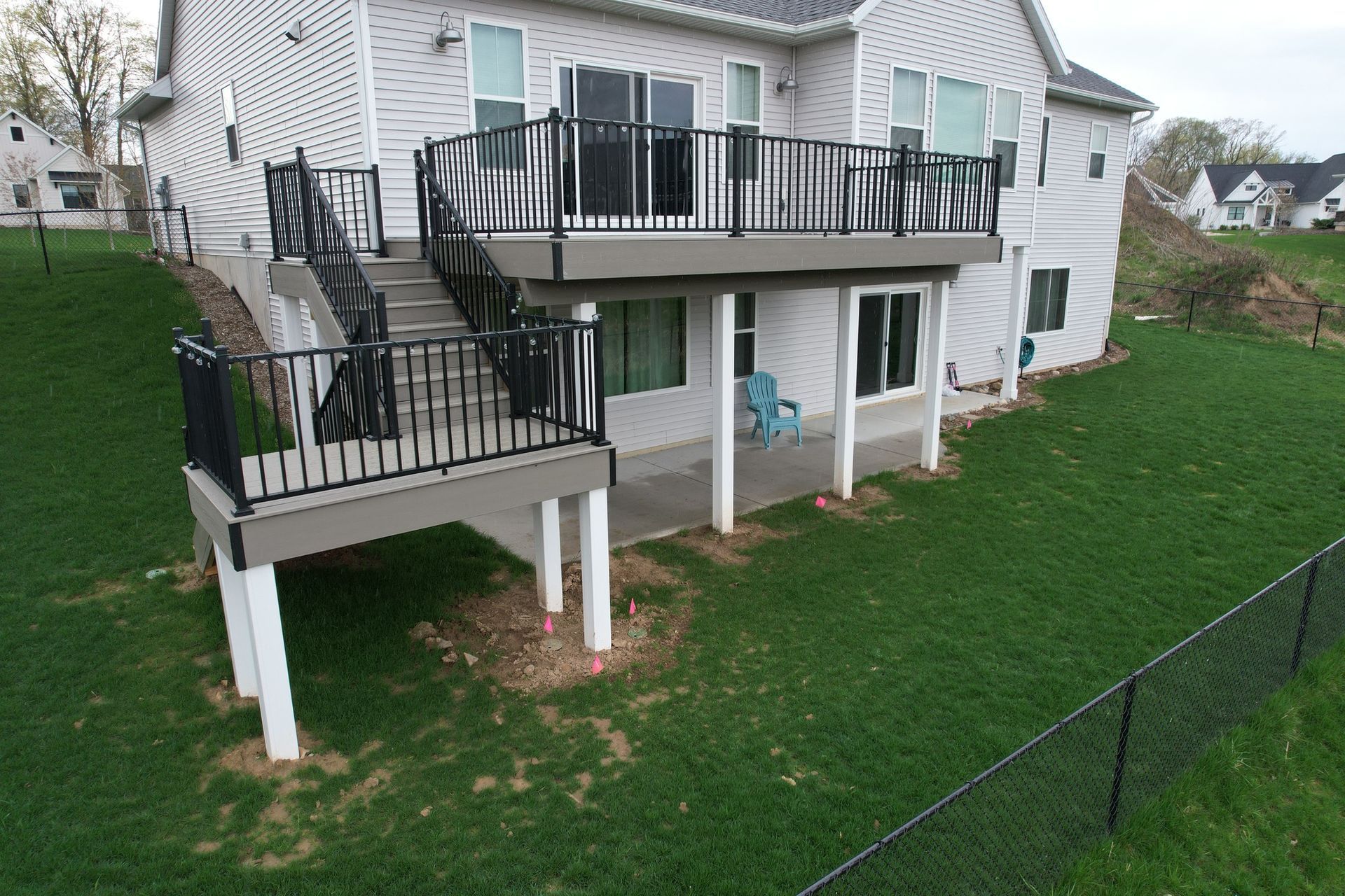 Two-story house with a deck and stairs overlooking a grassy yard with a black fence. The deck has black railing.
