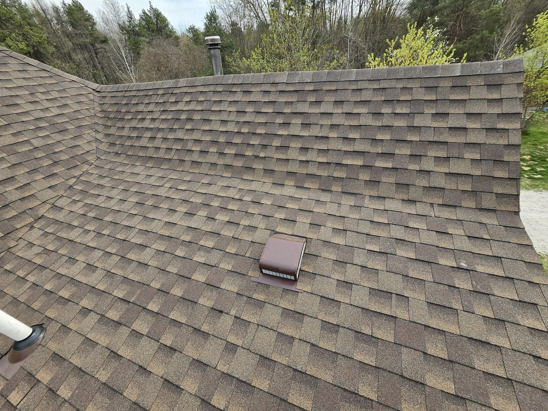 Close-up view of a brown shingled roof with a vent in the center and damaged shingles.