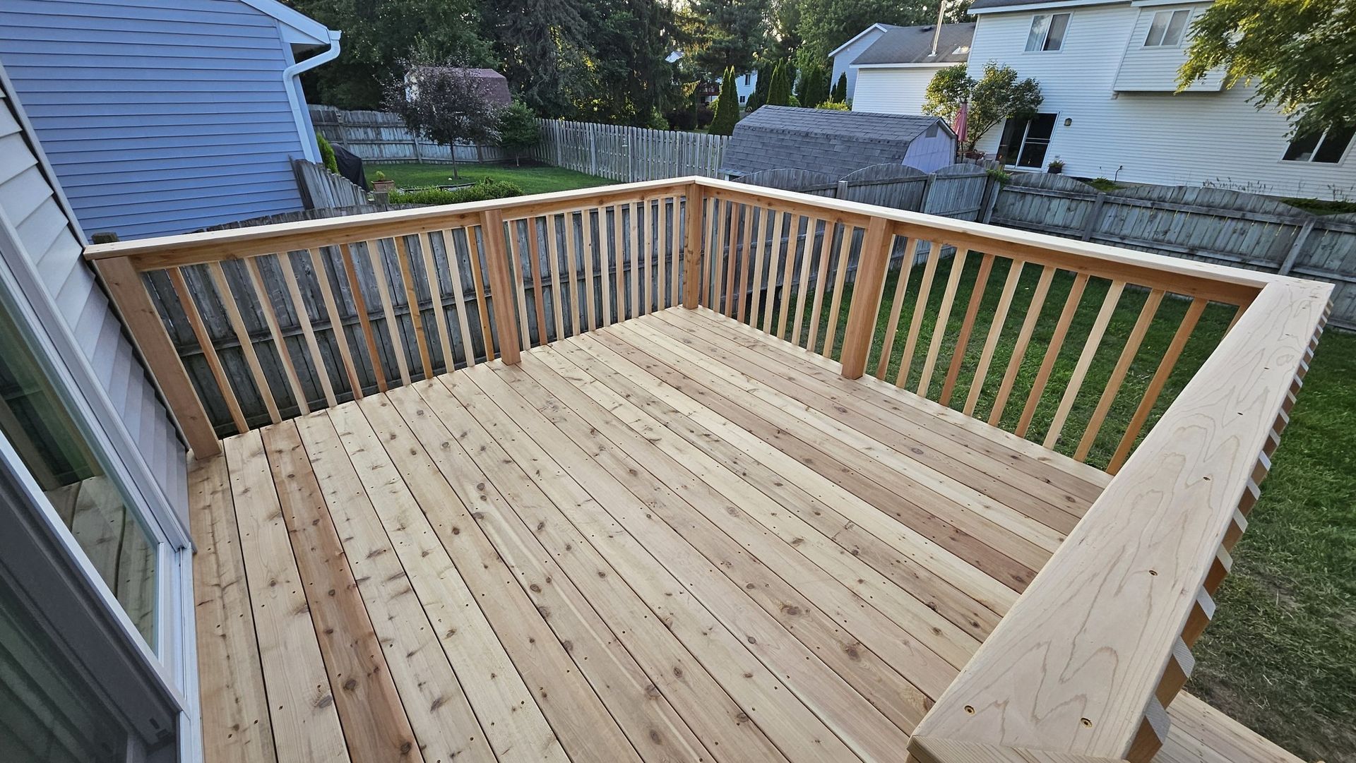Newly built wooden deck with railing, overlooking a grassy yard. The deck is light-colored and freshly constructed.