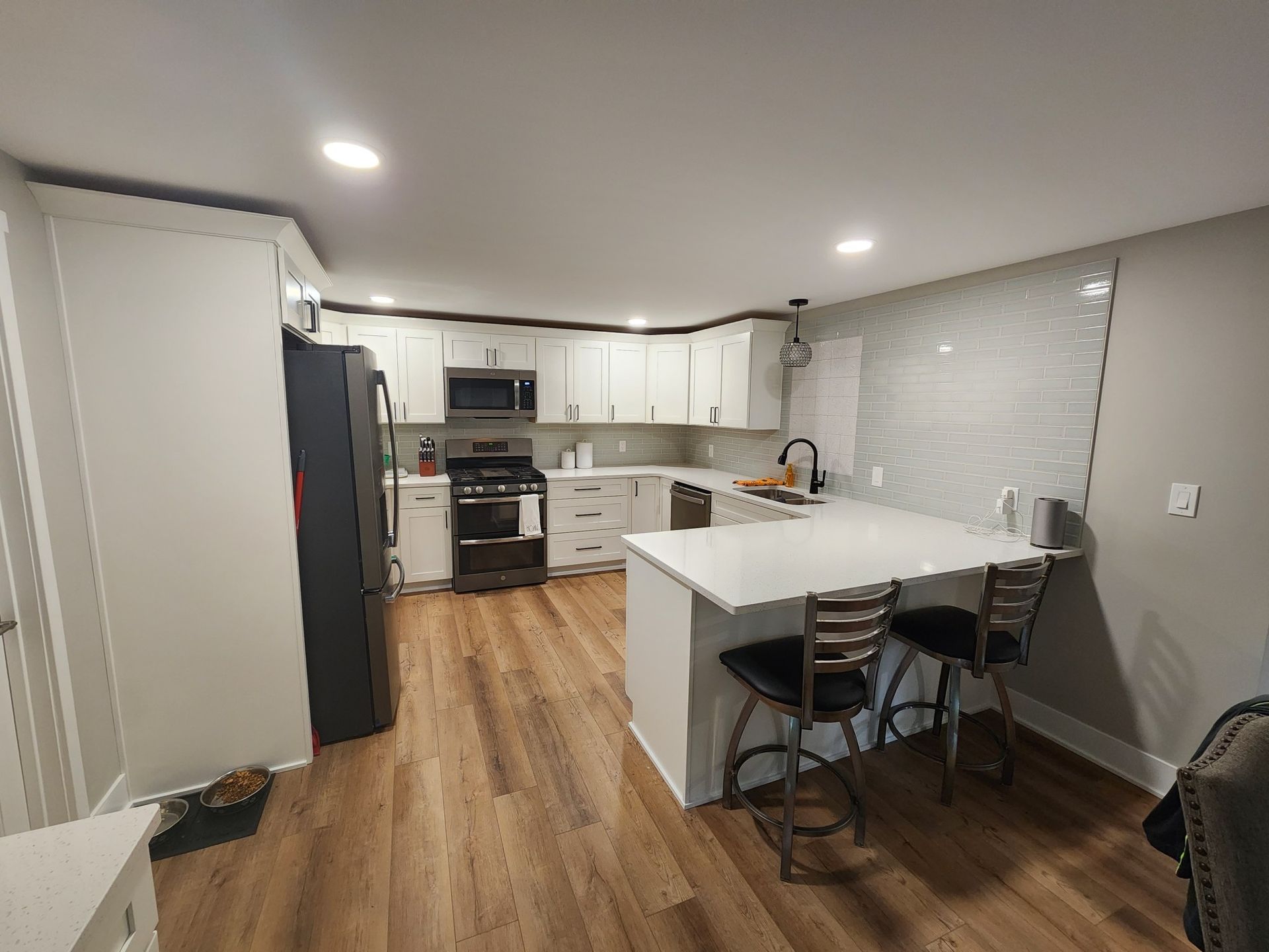 Modern kitchen with white cabinets, a breakfast bar with stools, and a dark refrigerator. Wooden floors and gray walls.