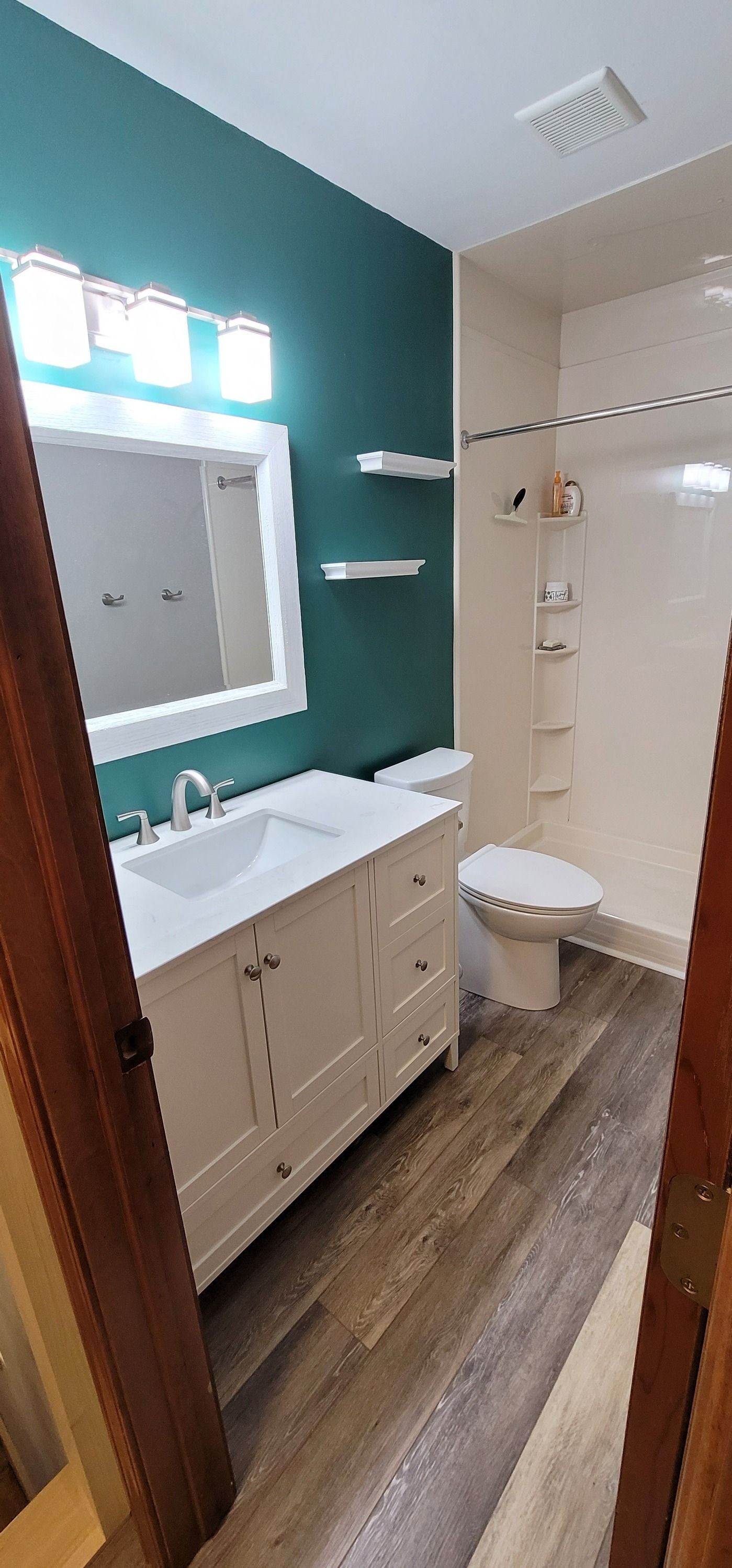A bathroom with a teal accent wall, white vanity, and neutral-toned flooring. A toilet and shower stall are also visible.