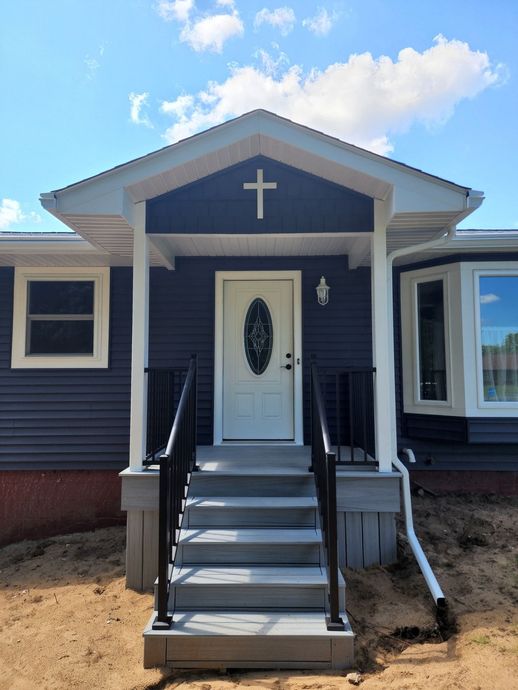A home with a white door and gray steps, topped with a porch featuring a cross. The house is navy blue with white trim.