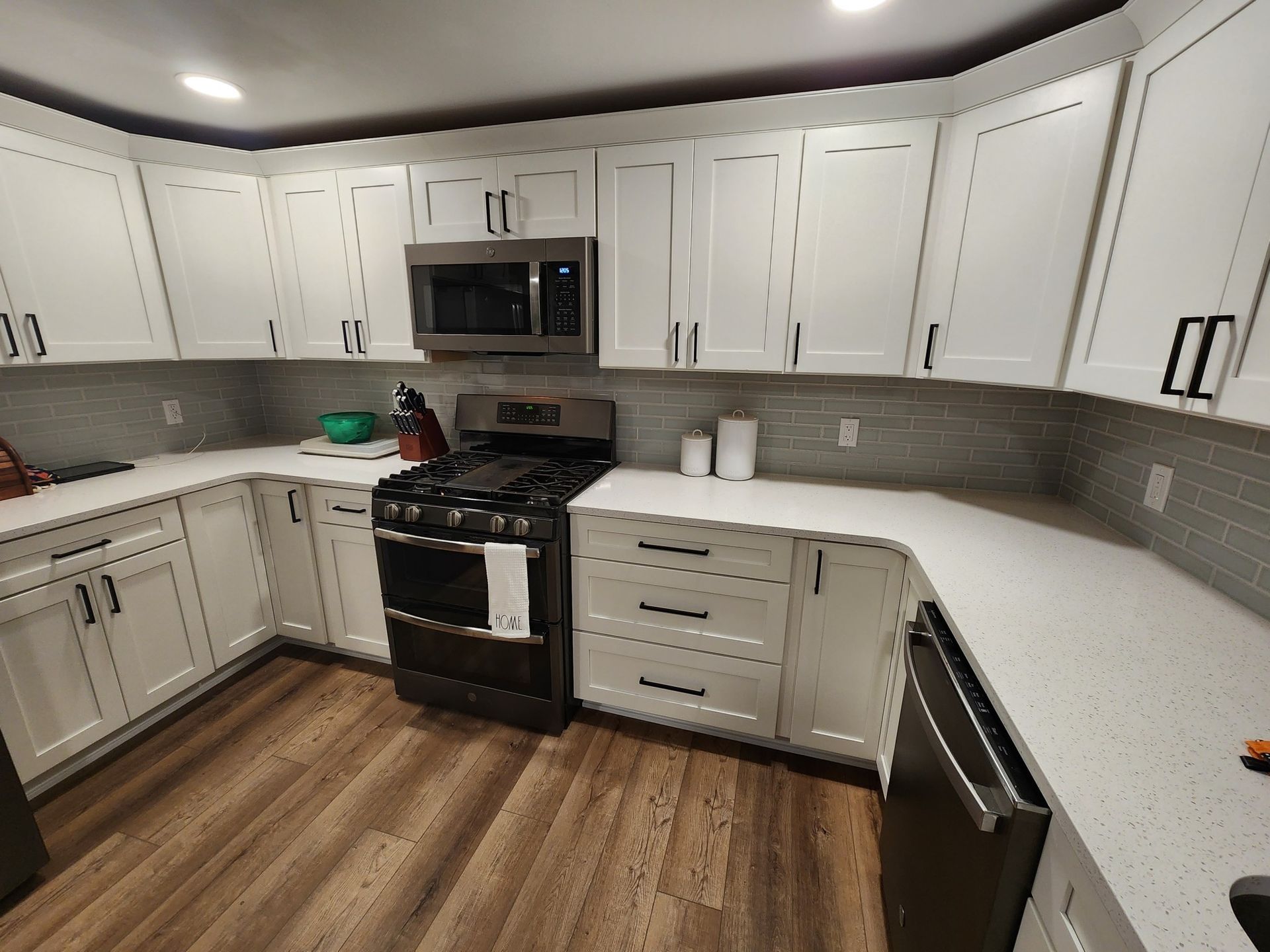 White kitchen with light wood floors, white cabinets, stainless steel appliances, and a gray backsplash.