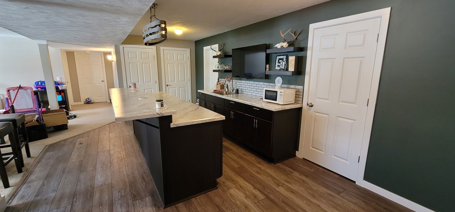 A kitchen with a dark island, white countertops, and dark cabinets. The walls are green and there is a door on the right.