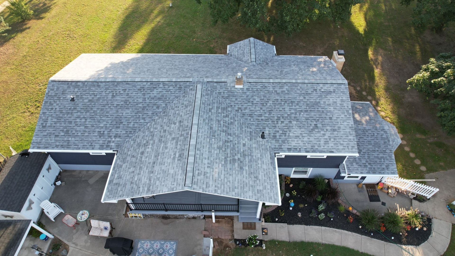 Aerial view of a house with a gray roof and blue siding, surrounded by green grass and a few trees.