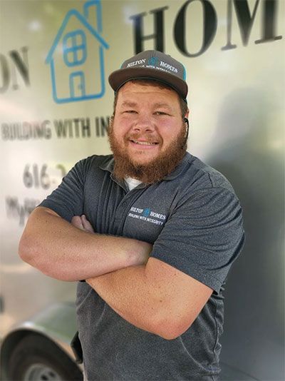 Man with a beard and ball cap, arms crossed, smiling in front of a trailer with a company logo.