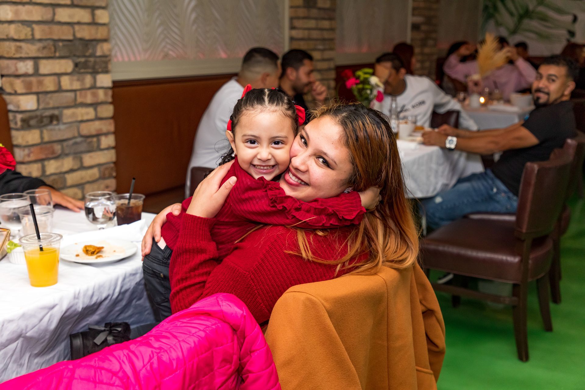 Woman hugging a child at a table in a restaurant. Both are smiling. Other people are seated nearby.