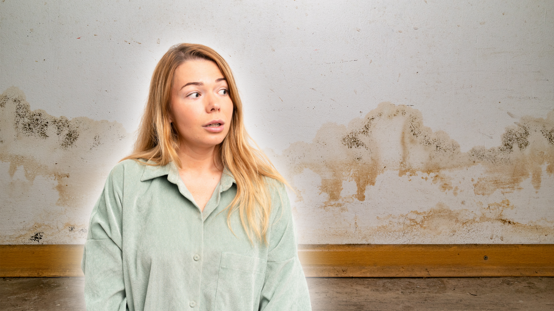 Woman with shocked expression stands before a moldy wall.