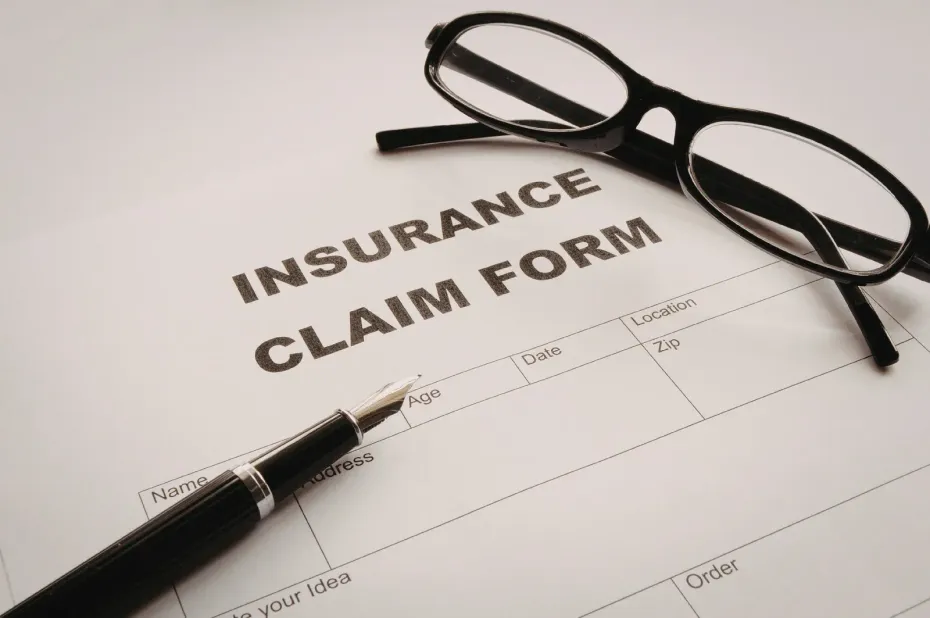 An insurance claim form with a fountain pen resting on it and a pair of black-rimmed glasses placed on top.