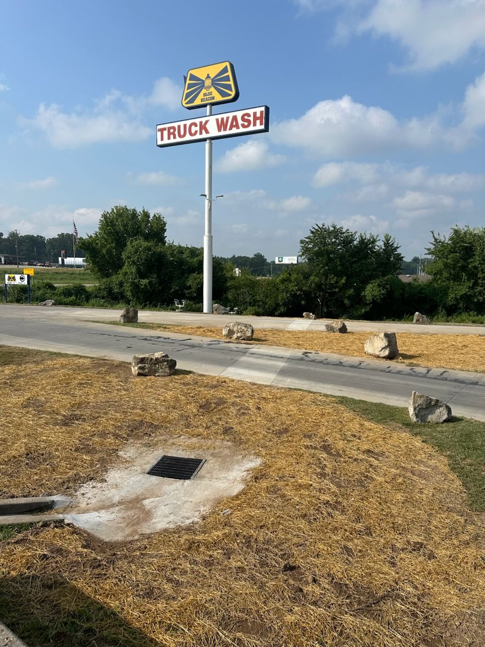 Truck wash sign beside a roadside lot under a blue sky, with dry grass and concrete curbs