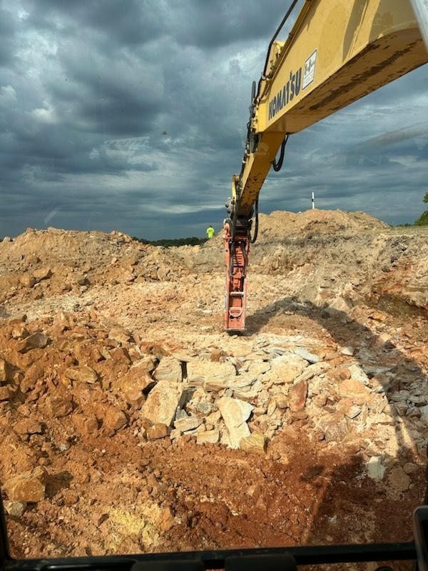 Excavator breaking rocky ground under dark storm clouds at a construction site