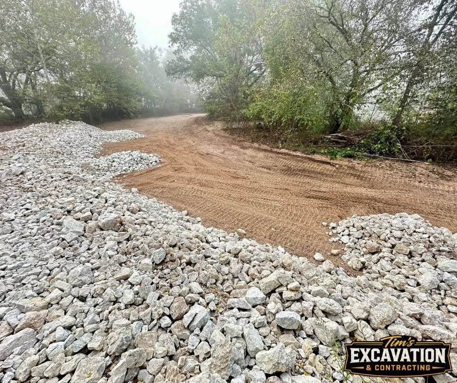 Rock-covered dirt road curving through a foggy wooded area with excavator work in the corner