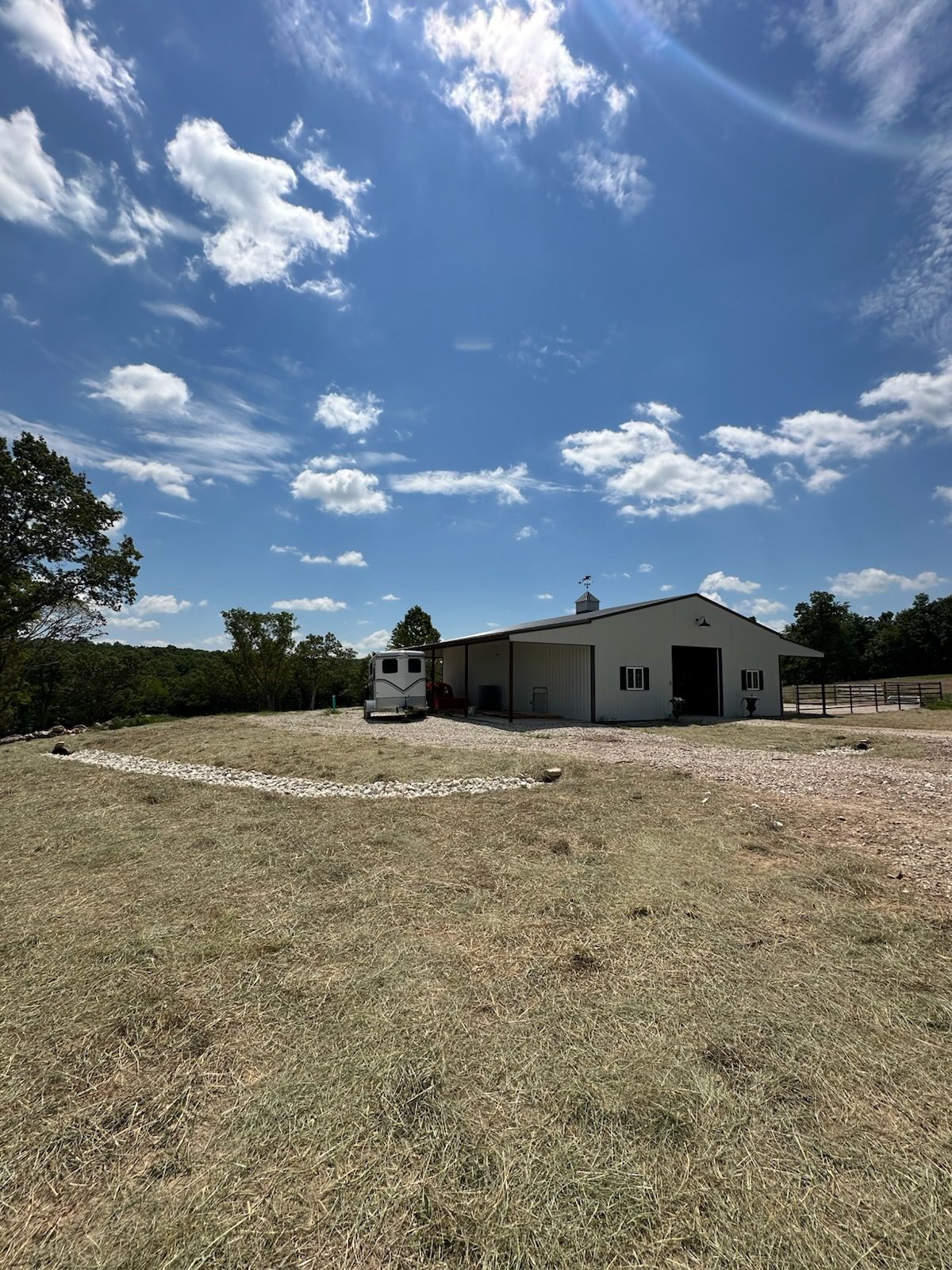 Rural house and outbuilding on a dry field under a bright blue sky with scattered clouds