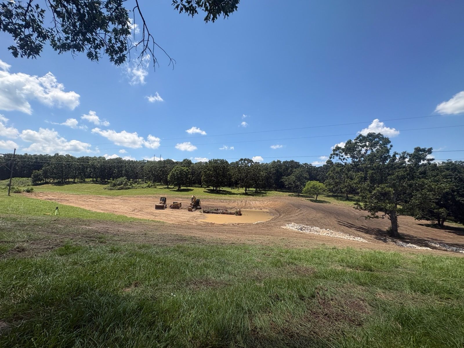 Sunny open field with a few people sitting near a fire pit under a blue sky and trees